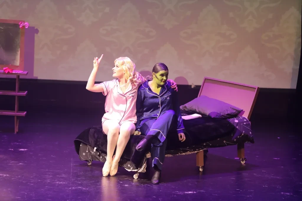 Two performers sitting on bed in stage scene
