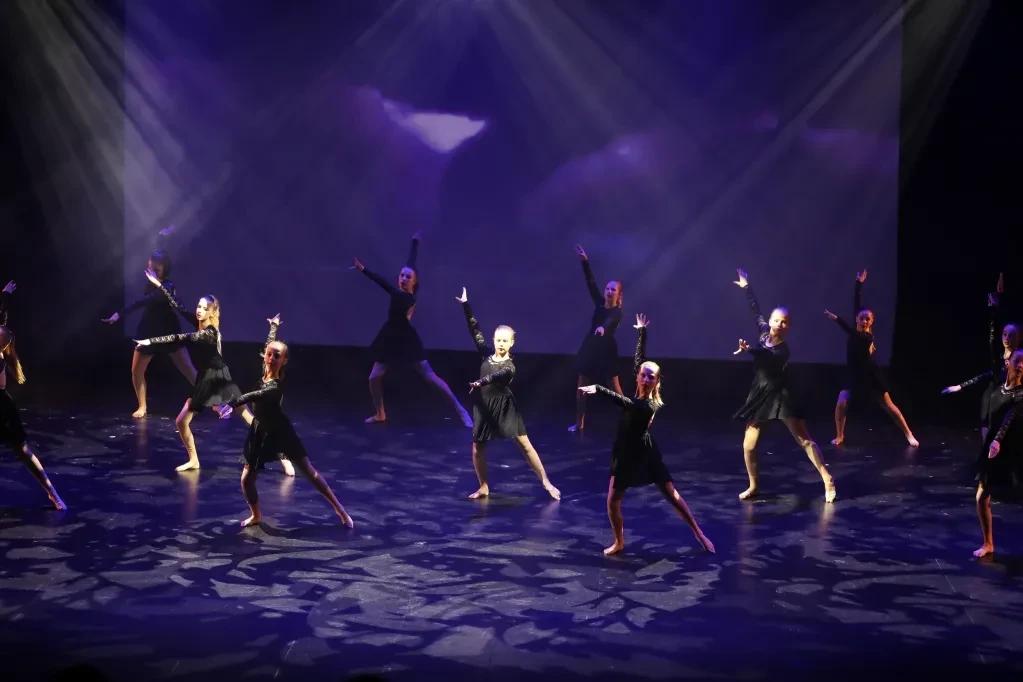 Dance ensemble performing on stage under purple lighting