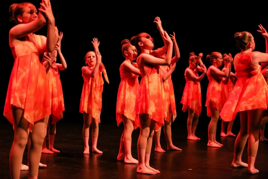 Large group of dancers in orange tie-dye dresses performing on stage