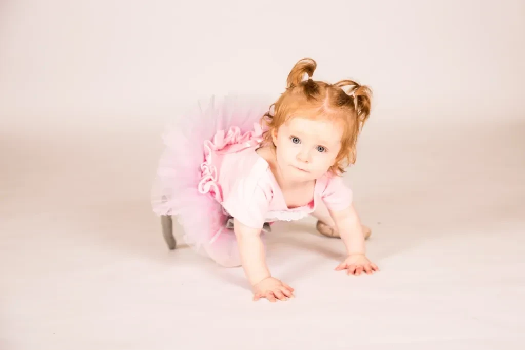 Baby in pink tutu crawling on white studio floor