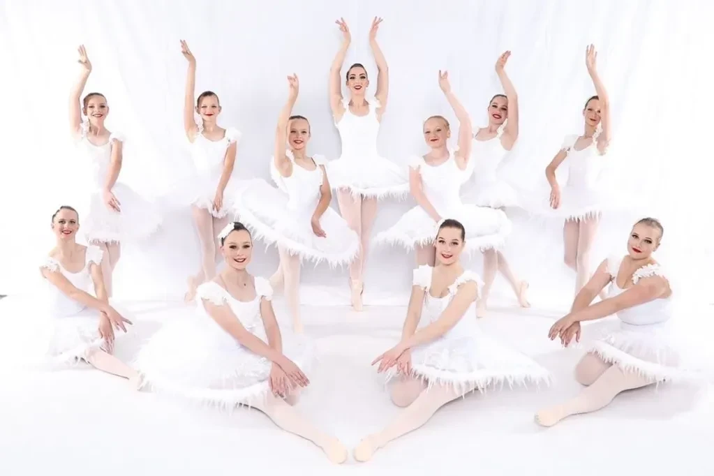 Large group of ballet dancers in white feathered tutus posed on white background