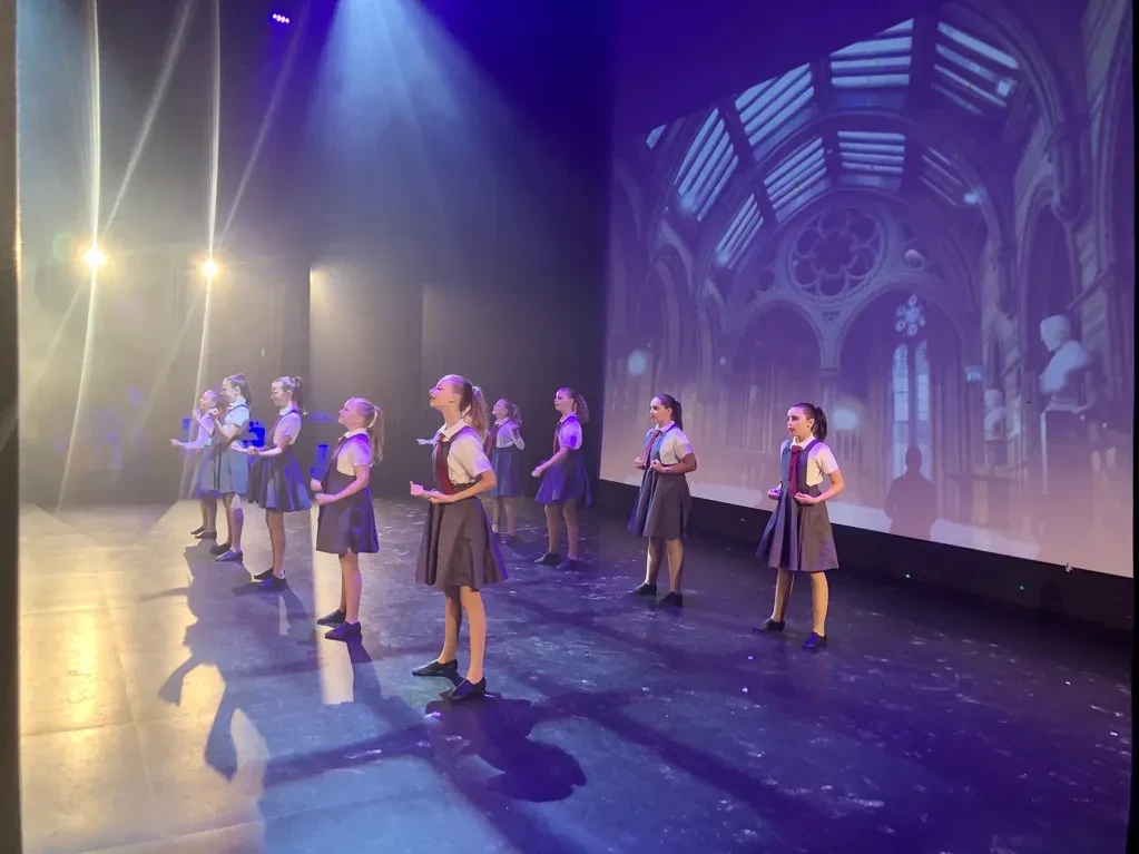 Children on stage in school uniforms with cathedral projected backdrop