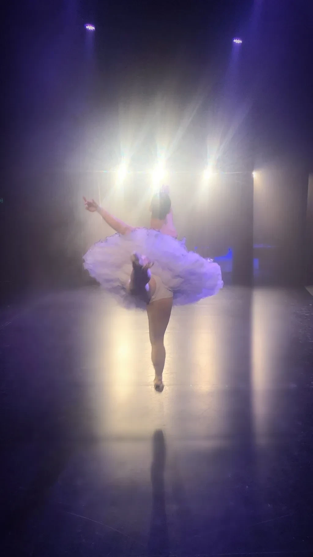 Dancer in lavender tutu spinning under dramatic stage spotlights