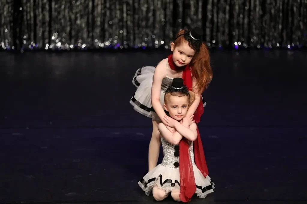 Two young children in black and white cabaret costumes with red scarves on stage