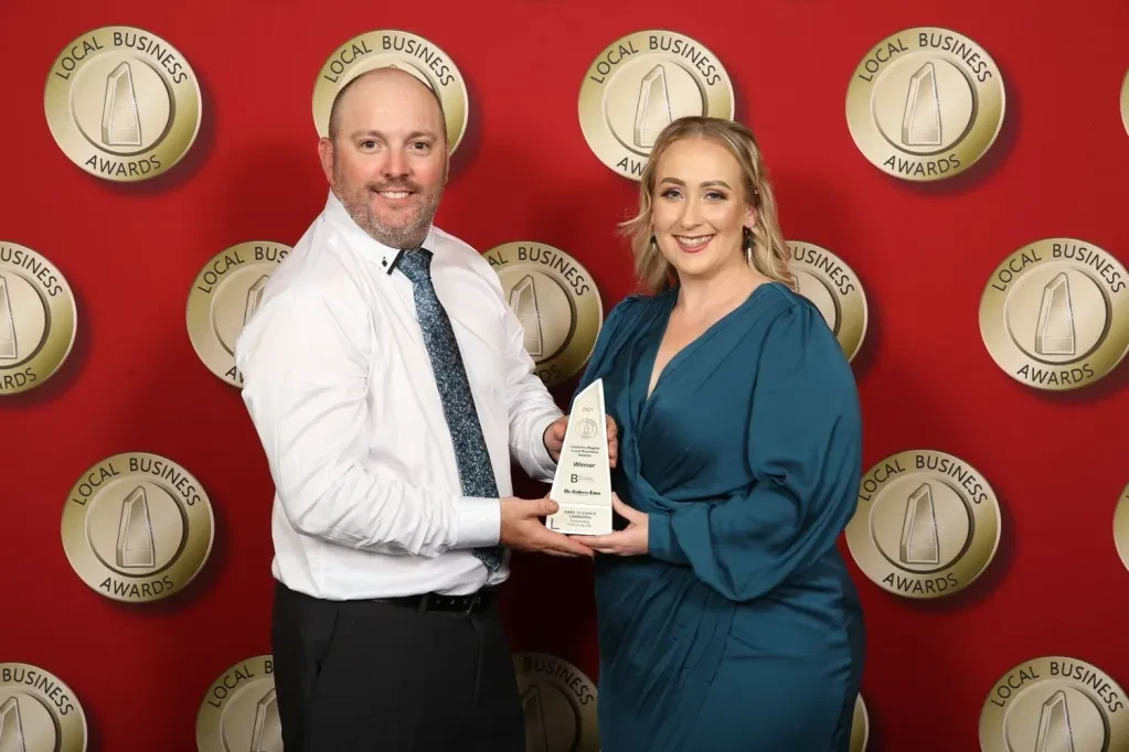 Two people jointly holding Local Business Awards winner trophy at awards ceremony