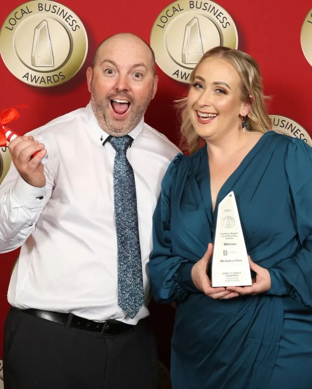 Excited pair celebrating Local Business Awards win with trophy at red carpet event