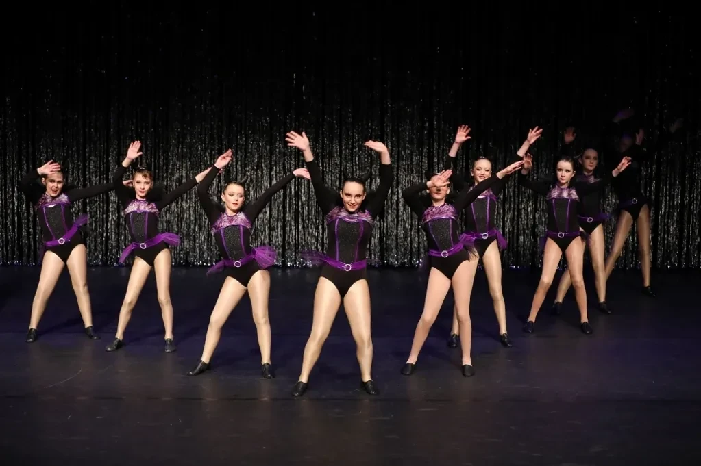 Dancers in black and purple jazz costumes performing in a line on stage